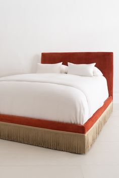 the bed is made up with white sheets and fringes on it's headboard