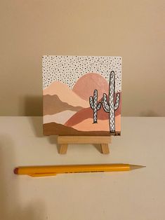 a small wooden easel with a painting on it next to a pencil