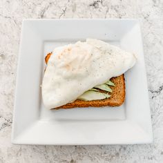 a white plate topped with an open face sandwich covered in sour cream and cucumbers