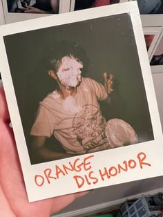 a person holding up a polaroid with an orange dis - honor on it