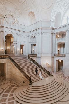 a bride and groom walking down the stairs in an ornate building