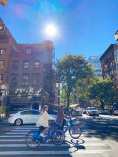 two people riding bikes across a cross walk