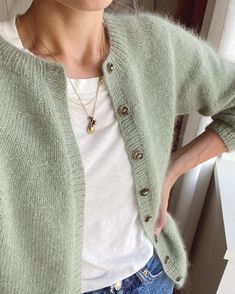 a woman standing next to a window wearing a green cardigan