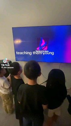 several people standing in front of a large television screen with the words teaching them young on it