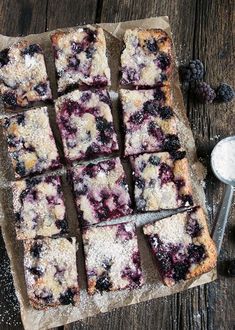 blueberry bars cut into squares with powdered sugar and berries on the table next to them