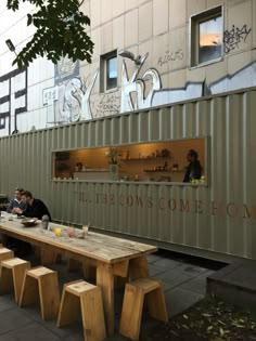 two people sitting at a table in front of a shipping container with writing on it