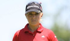 a woman in a red shirt and black hat is standing with her golf club cap on