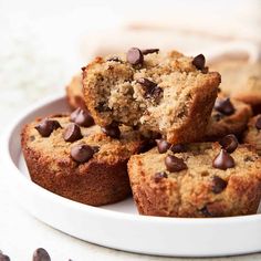 chocolate chip muffins stacked on top of each other in a white plate with more muffins nearby