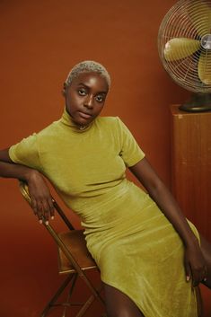 a woman in a yellow dress sitting on a chair next to a table with a fan