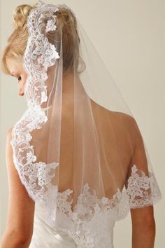 the back of a bride's wedding dress with a veil on her head and shoulder