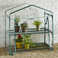 a green house with potted plants in it on top of a gravel floor next to a white brick wall