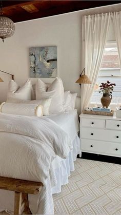 a white bed sitting in a bedroom next to a window with curtains on the windowsill