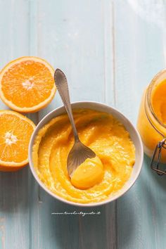 a spoon in a bowl with oranges next to it on a blue table top