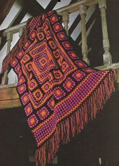 a crocheted shawl hanging on a wooden railing with pink and orange colors