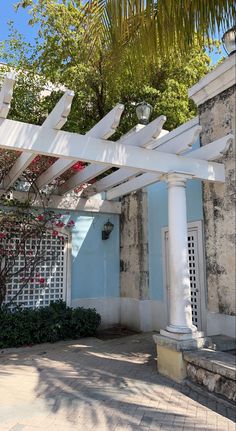 a white pergolated structure in front of a blue building with trees and bushes