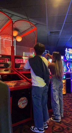 two people are standing in front of a pinball machine at an indoor game room