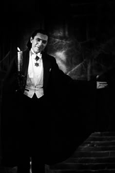 a man in a tuxedo holding a candle and posing for a black and white photo