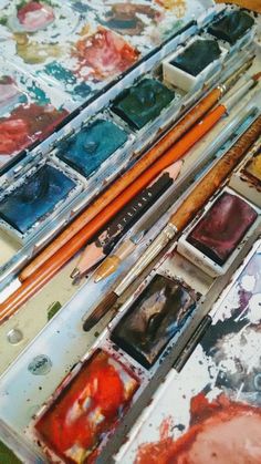 an artist's palettes and brushes are sitting on a table covered in watercolor paints