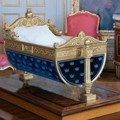 a miniature bed with blue and gold paint on it's sides, sitting on a wooden table