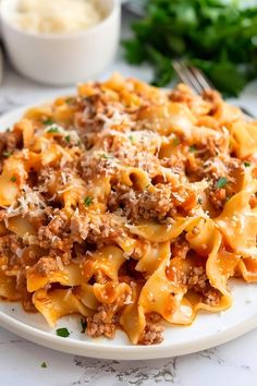 a white plate topped with pasta covered in ground beef and parmesan cheese next to a bowl of mashed potatoes