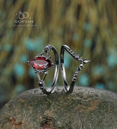 two silver rings with red stones on top of a rock