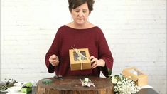 a woman is holding a box with flowers on it while standing next to a tree stump