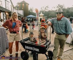 a man, woman and two children in a cart at an outdoor event with people standing around