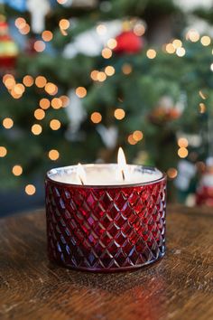 a red glass candle sitting on top of a wooden table next to a christmas tree