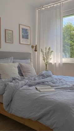 a bed with blue sheets and pillows in a bedroom next to a large window on the wall