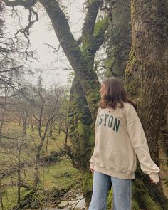 a woman standing in front of a tree with moss growing on it's branches