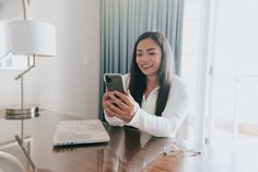 a woman sitting at a table looking at her cell phone while holding it in one hand