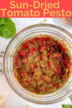 sun dried tomato pest in a glass bowl with basil leaves and garlic on the side