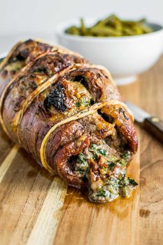 a meatloaf roll on a cutting board next to a bowl of green beans