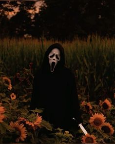 a person in a black hoodie with a white mask on standing in a field of sunflowers