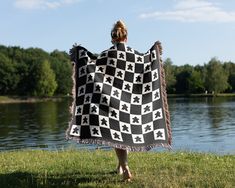 a woman is holding up a black and white checkerboard blanket by the water