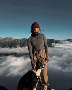 a woman standing on top of a mountain with her dog