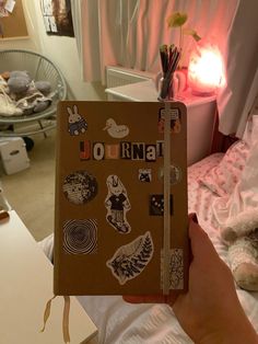 a person holding up a journal with stickers on it in front of a bed