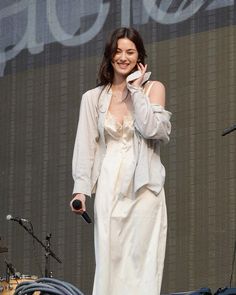 a woman in a white dress talking on a cell phone while standing next to a microphone