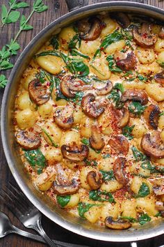 a pan filled with pasta and mushrooms on top of a wooden table next to silverware