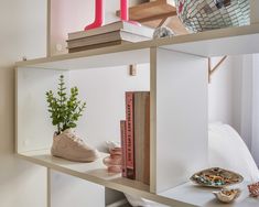 a shelf with books, plants and other items on it in a room that has white walls