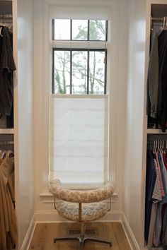 a chair sitting in front of a window next to a closet filled with coats and jackets