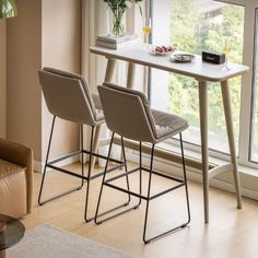 two chairs sitting at a table in front of a window with a vase on it