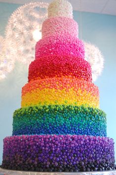 a multi - colored cake with sprinkles on it is displayed in front of a chandelier