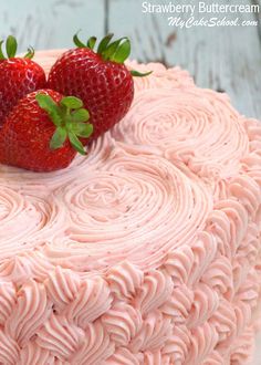 two strawberries on top of a pink frosted cake with icing spirals