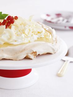 a cake with white frosting and red berries on top sits on a plate next to silverware