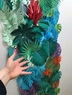 a person reaching out to touch a wall made from paper flowers and palm leaf shapes