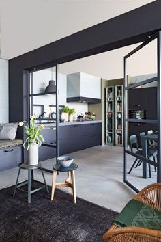 an open kitchen and dining area with black cabinets, white walls and flooring is seen from the living room