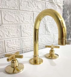 two gold faucets on a white countertop in front of a brick wall