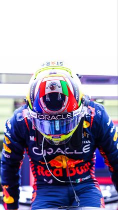 a man in a racing suit and helmet sitting on top of a race car while listening to headphones