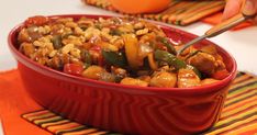 a red bowl filled with food sitting on top of a colorful place mat next to an orange napkin